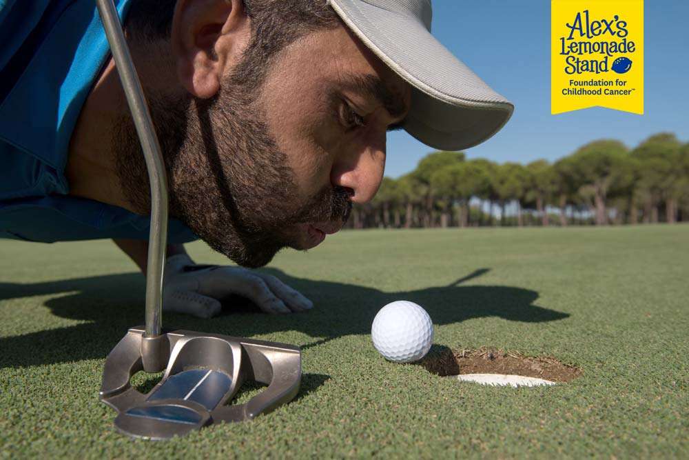 Humorous photo of man trying to blow a golf ball into the hole